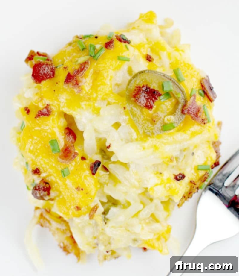 Kickin' Hash Brown Popper Casserole 5 Close-up shot of a spoonful of creamy, cheesy potato casserole on a white plate, showcasing its rich texture and toppings.