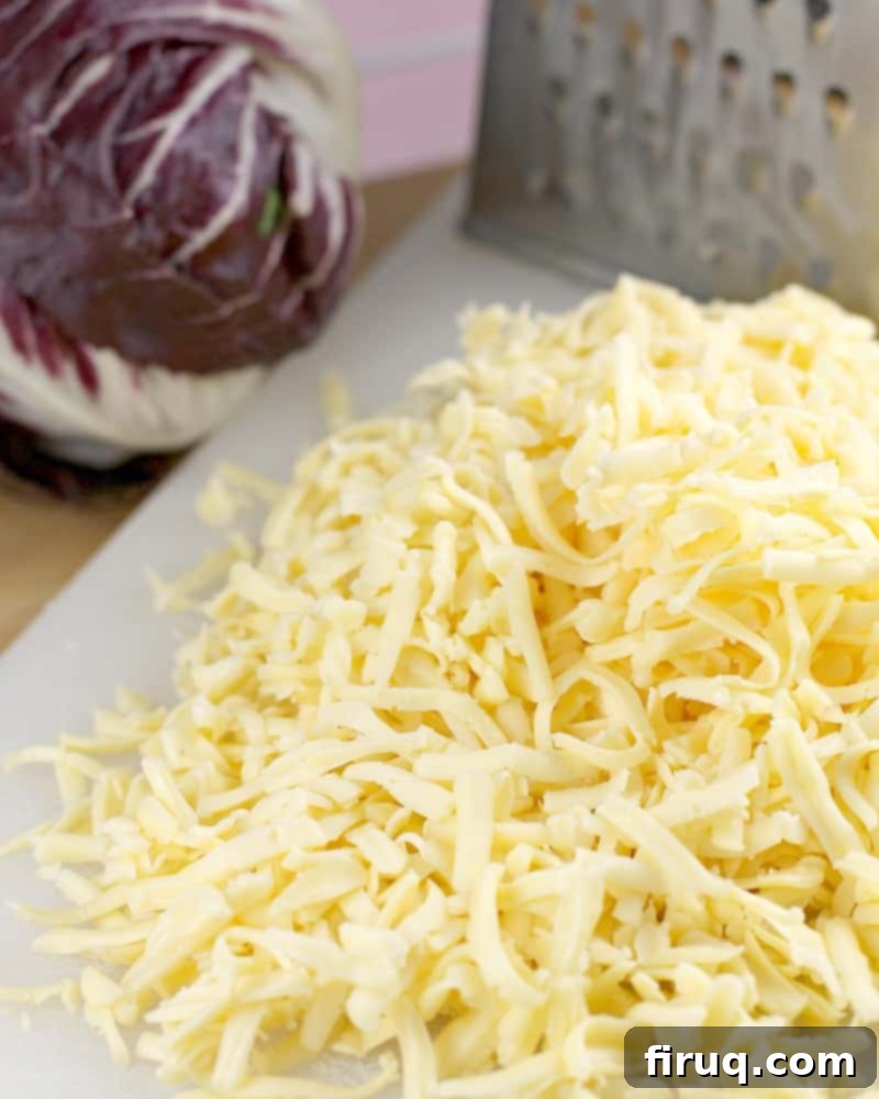 Imperial Russian Garlic Cheese 4 A generous pile of freshly shredded Havarti cheese, with a grater and radicchio in the background, showcasing the key ingredient for this easy Russian cheese spread.