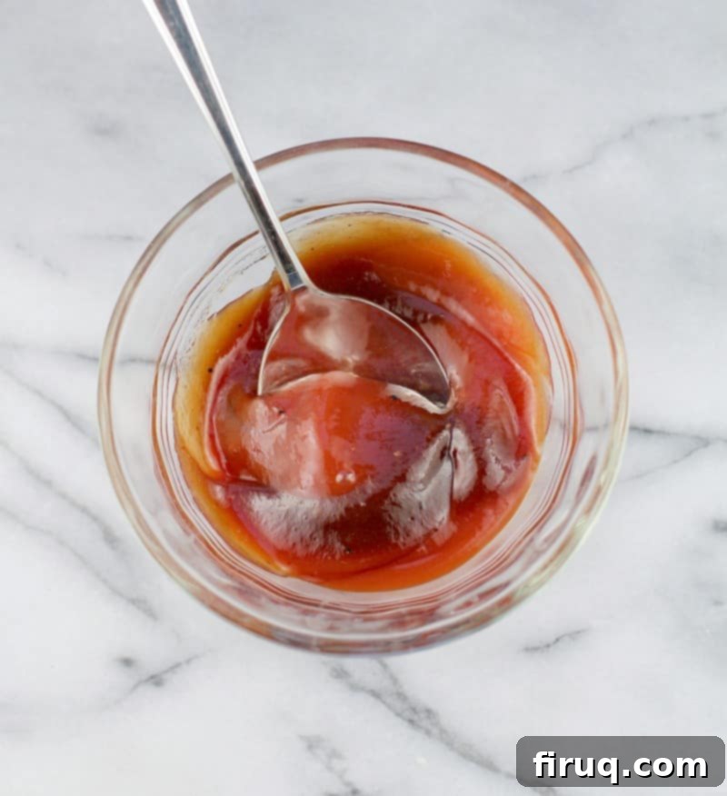 Mom's Meatloaf 6 top down view of a spoon mixing the ketchup and barbecue sauce in a clear glass bowl on a marble surface