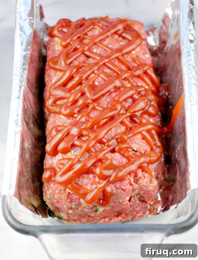 Mom's Meatloaf 7 the prepared meatloaf topped with the ketchup mixture in a clear glass loaf pan lined with foil