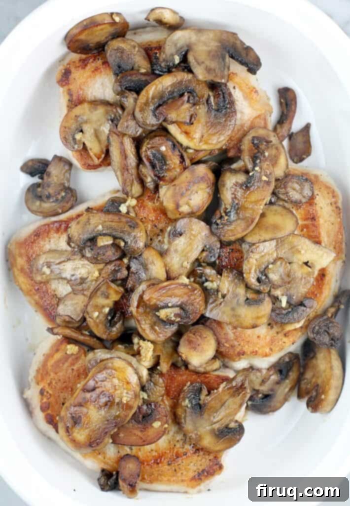 Hearty Pork Chop and Cornbread Bake 8 top view of browned mushrooms on the seared chops in a white bake dish