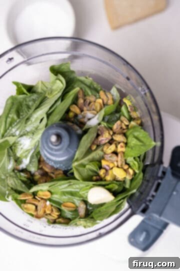 Emerald Pistachio Pesto 4 Fresh basil, shelled pistachios, a clove of garlic, salt, and lemon juice in the bowl of a food processor, ready to be blended.