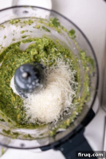 Emerald Pistachio Pesto 7 Freshly grated Parmigiano-Reggiano cheese being added to the finished pistachio pesto in the food processor.