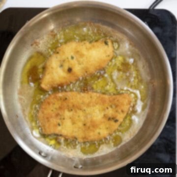 Crispy Golden Italian Chicken Cutlets 11 Chicken cutlets frying in oil, with one recently flipped to reveal a golden-brown side.