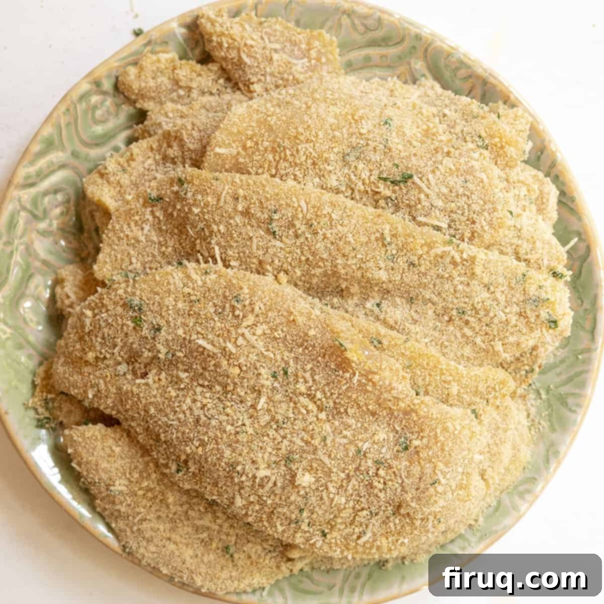 Crispy Golden Italian Chicken Cutlets 13 A pile of uncooked chicken breasts dredged in seasoned breadcrumbs, ready for frying.