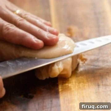 Crispy Golden Italian Chicken Cutlets 5 A hand thinly slicing a chicken breast on a cutting board, preparing it for a cutlet.
