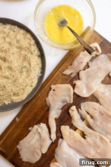 Crispy Golden Italian Chicken Cutlets 7 A breading station set up with thinly sliced chicken, a bowl of whisked eggs, and a plate of seasoned breadcrumbs.