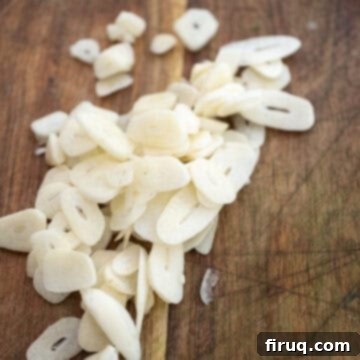 Grandma's Traditional Sunday Gravy 4 Garlic sliced thin on a cutting board.
