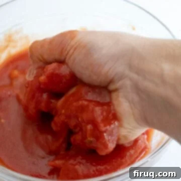 Grandma's Traditional Sunday Gravy 5 Hand crushing tomatoes in a bowl.