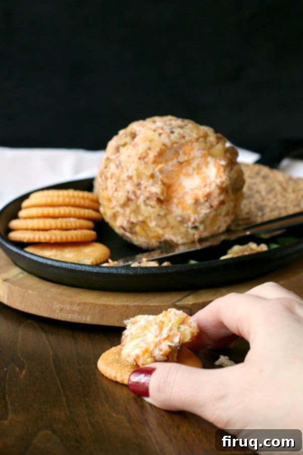 Serving Easy Cheddar Walnut Cheese Ball A hand taking a cracker topped with homemade cheese ball.