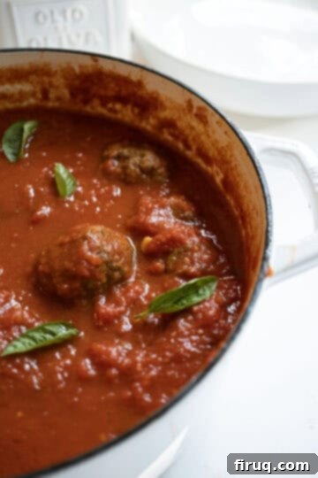 Nonna's Crispy Italian Meatballs 11 A pot filled with sauce and meatballs, garnished with basil.
