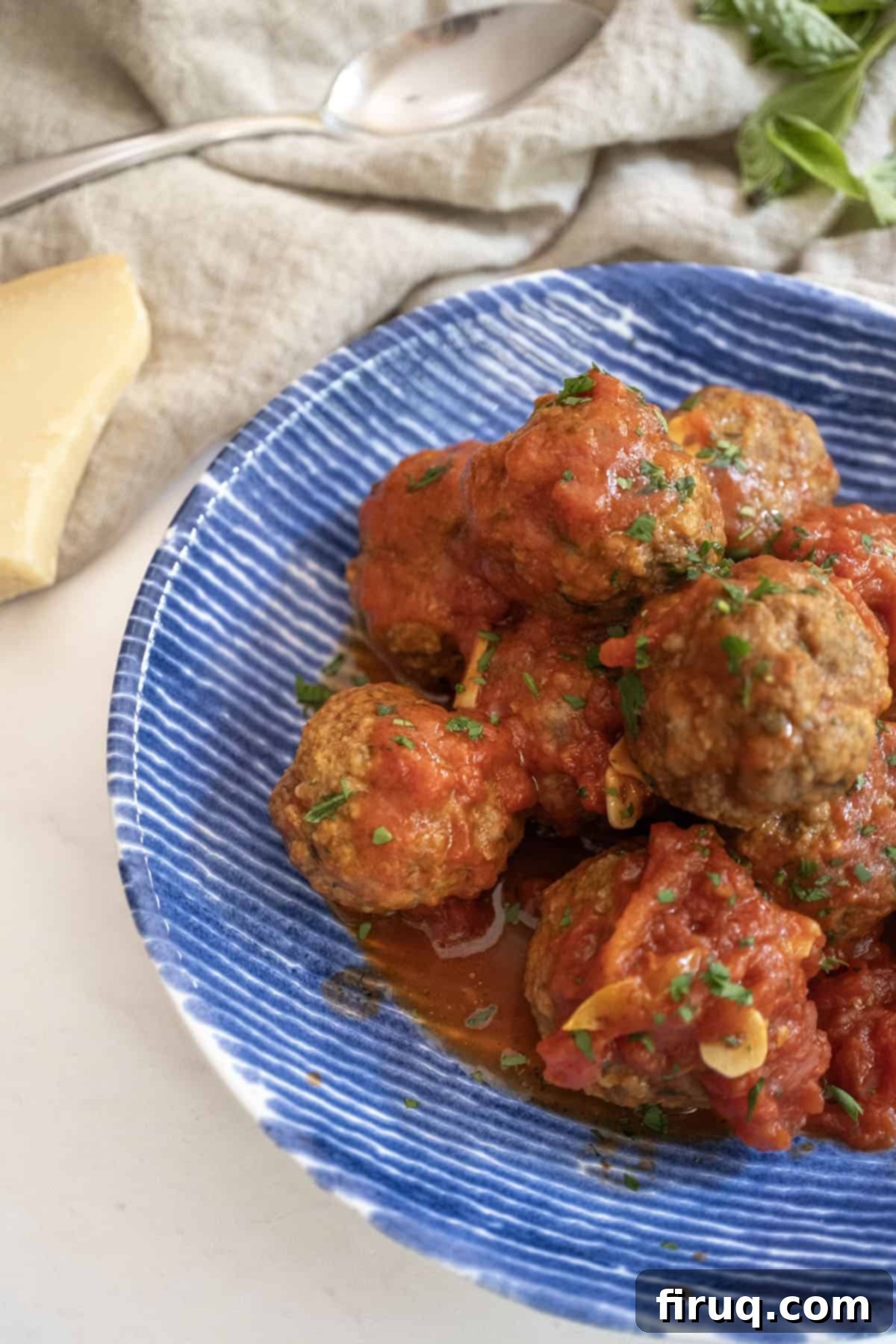 Nonna's Crispy Italian Meatballs 12 Meatballs covered in tomato sauce in a bowl with a block of parmesan cheese on the side.