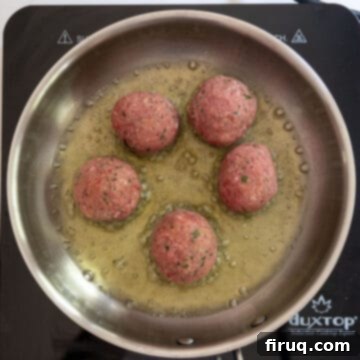 Nonna's Crispy Italian Meatballs 6 Frying raw meatballs in a saucepan.