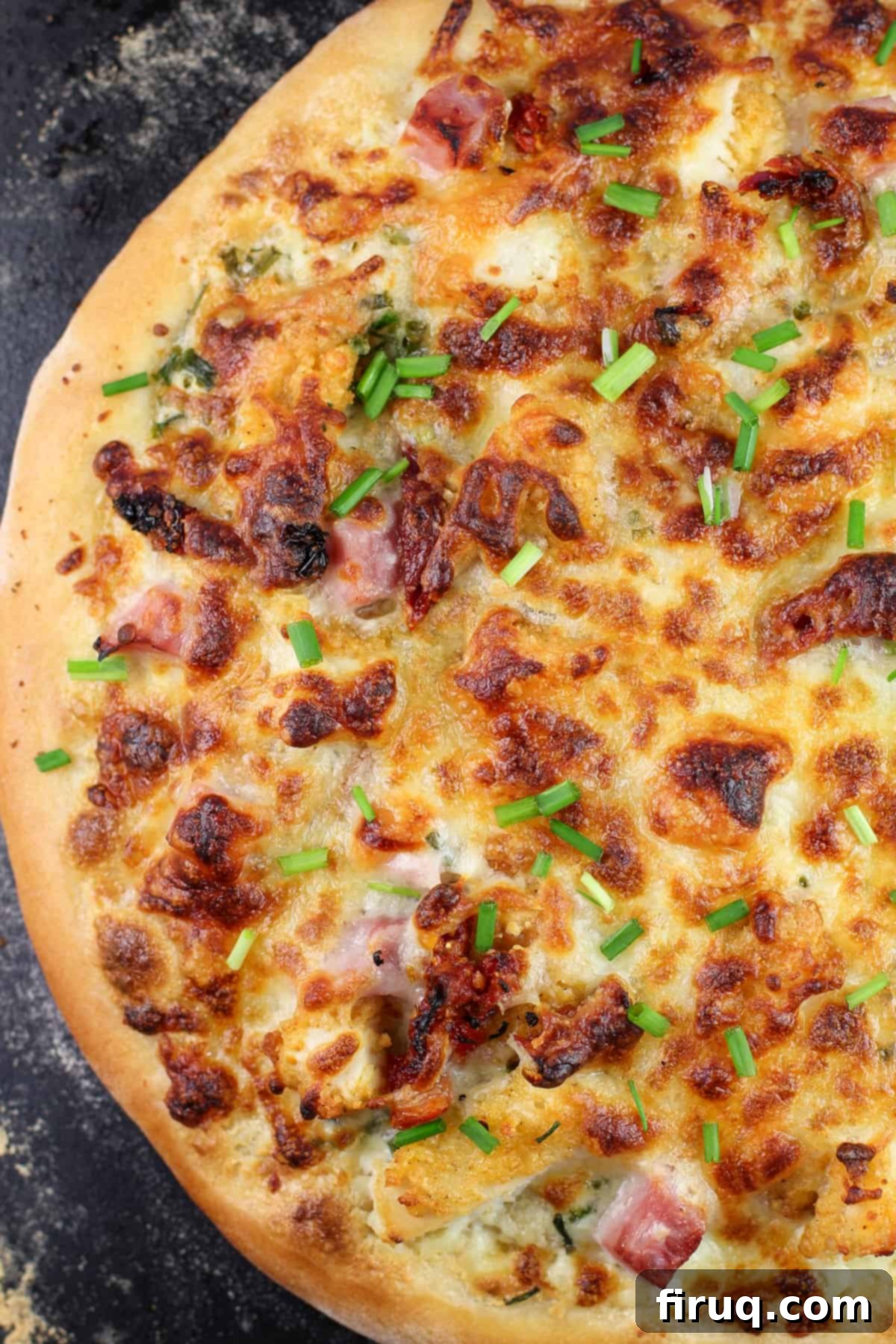 Chicken Cordon Bleu Pizza 3 Whole cooked chicken cordon bleu pizza resting on a black pizza stone, ready to be sliced and served.