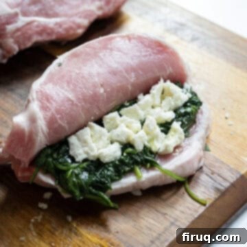 The Ultimate Grilled Stuffed Pork Chops 7 A raw butterflied bone-in pork chop generously stuffed with the savory sauteed spinach and crumbled feta cheese mixture, ready for grilling.
