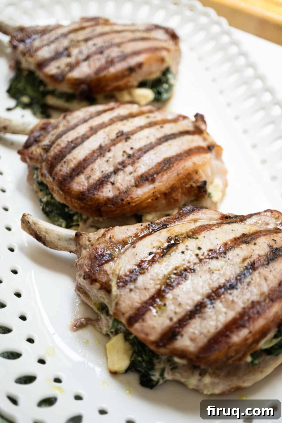The Ultimate Grilled Stuffed Pork Chops 10 Three perfectly grilled stuffed pork chops with golden-brown grill marks, overflowing with melted feta and vibrant spinach, served on a rustic cutting board.