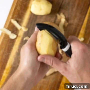 Crispy Hash Browns Perfection 4 A person peeling potatoes over a cutting board, preparing them for grating.