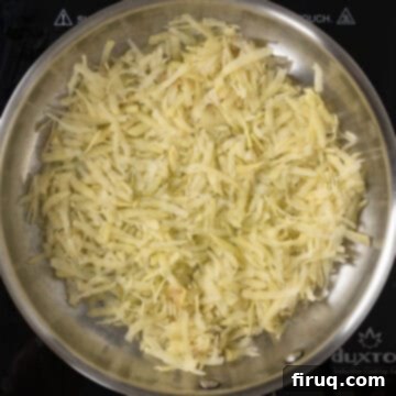 Crispy Hash Browns Perfection 8 A thin, single layer of grated potatoes frying in a large pan with olive oil.