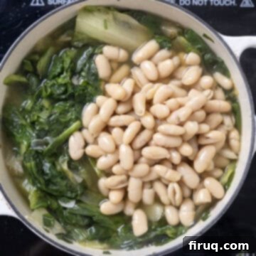 Hearty Escarole and Bean Soup 7 Cannellini beans and chicken broth poured into the Dutch oven with wilted escarole, ready to simmer and infuse flavors.