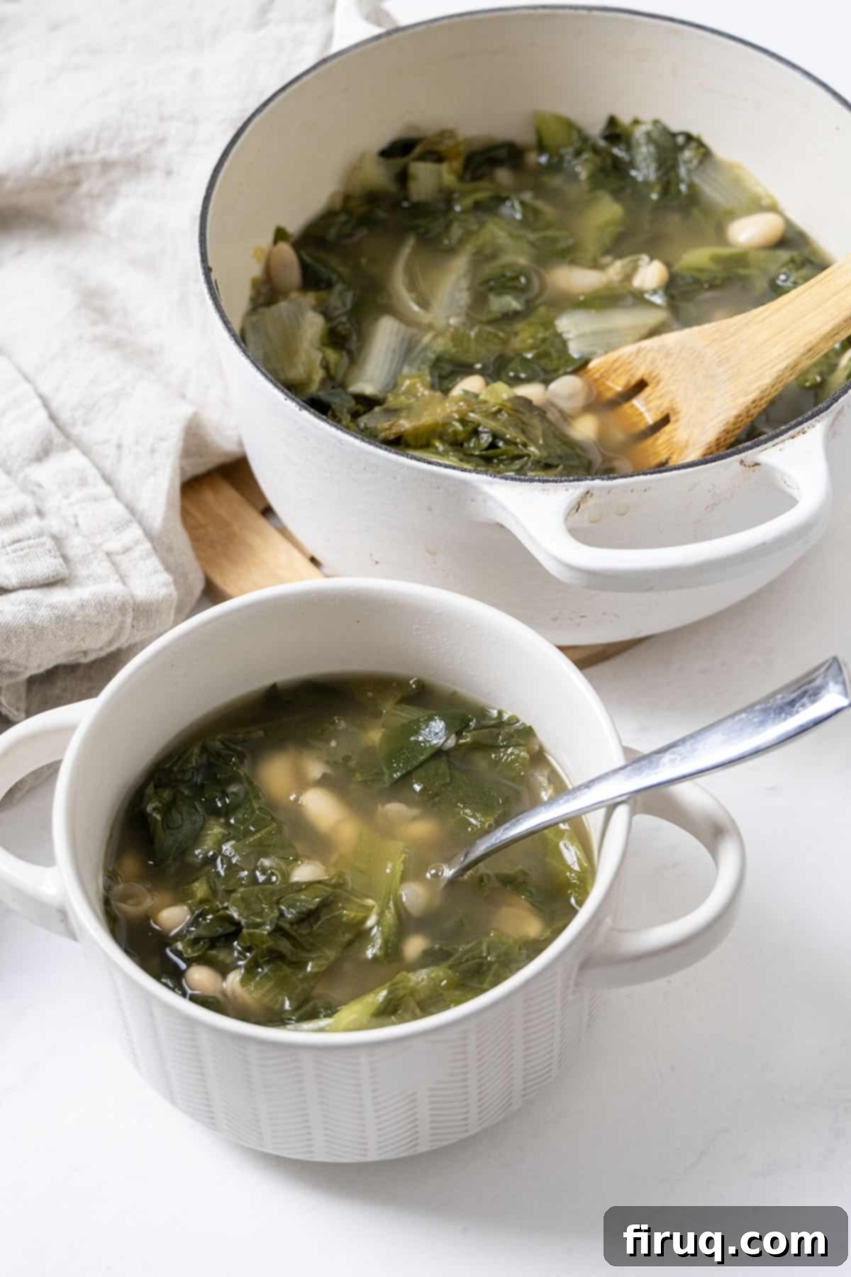 Hearty Escarole and Bean Soup 9 A beautifully presented bowl of Escarole and Bean Soup, garnished with fresh grated Parmesan cheese and a sprig of fresh herbs, beside the large Dutch oven, inviting viewers to enjoy this comforting dish.