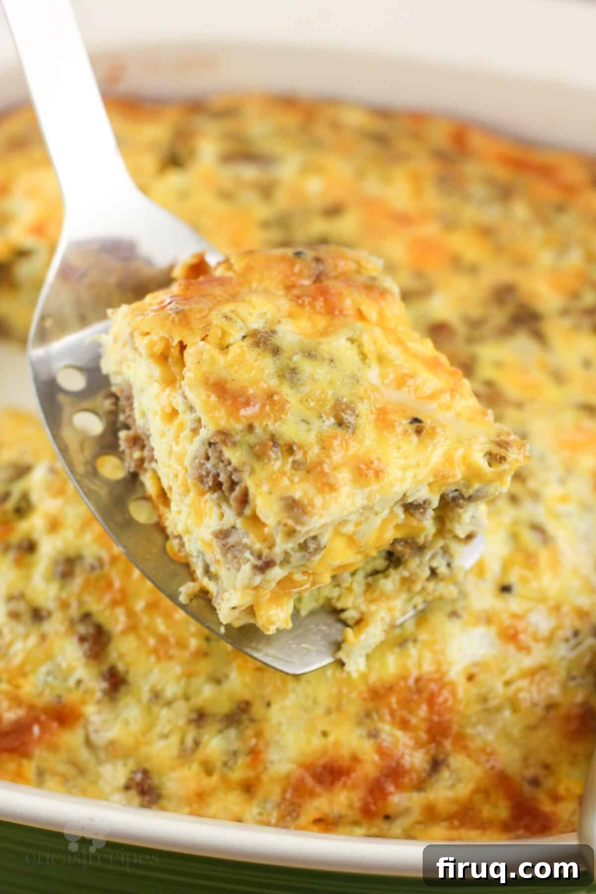 Hearty Sausage & Vegetable Bake 7 A spatula lifting a perfectly square portion of baked sausage egg and cheese casserole from the green baking dish, showing its texture.