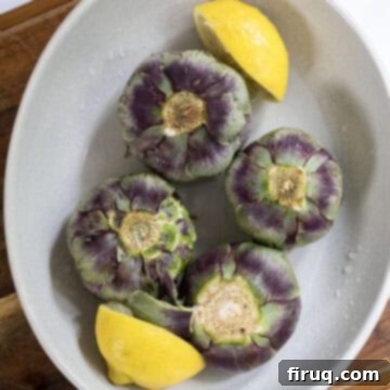 Simple Italian Stuffed Artichokes 4 Artichokes soaking in lemon juice in a bowl.