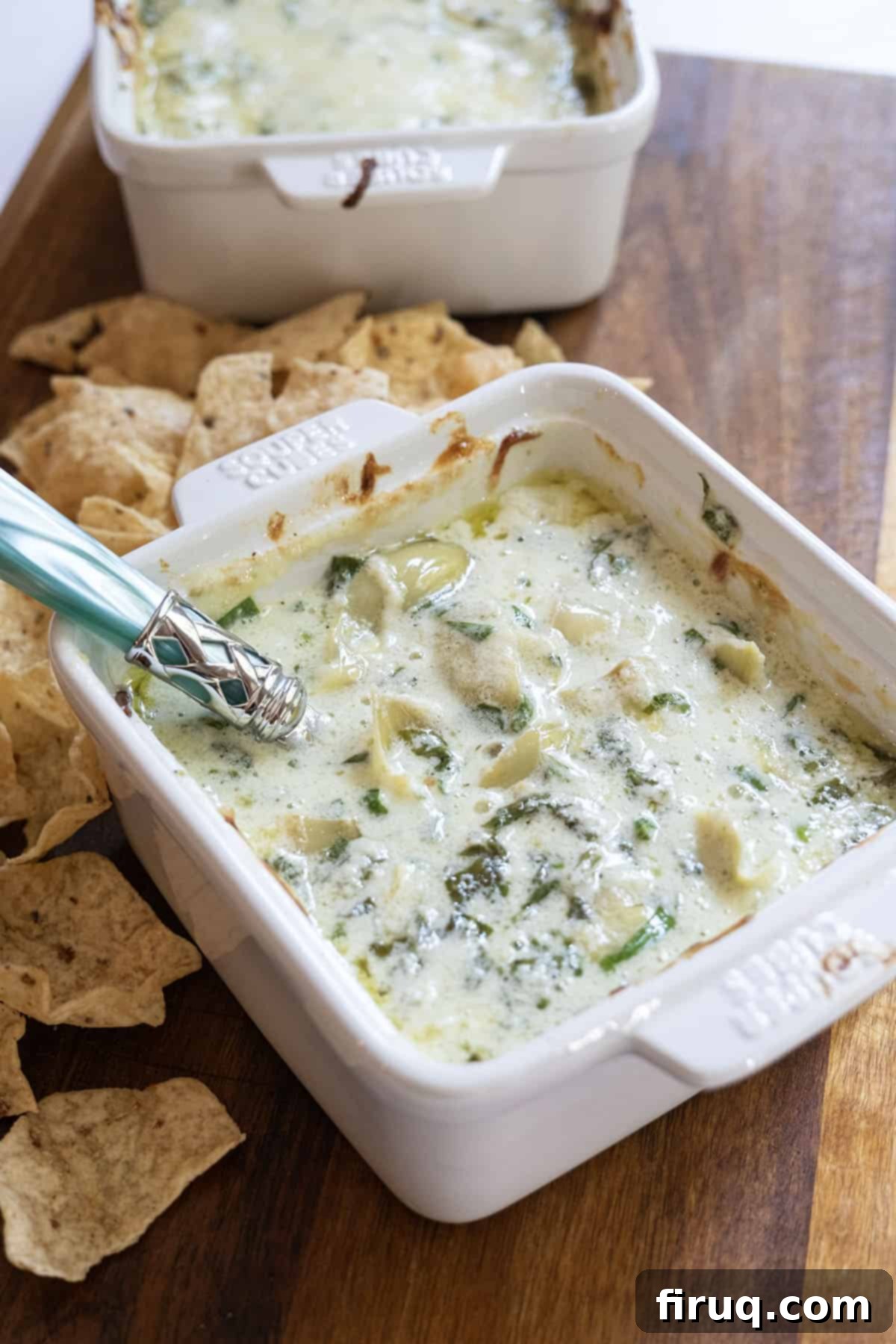 Guilt-Free Creamy Spinach Artichoke Dip 2 Spinach and artichoke dip in a dish with some tortilla chips next to it.