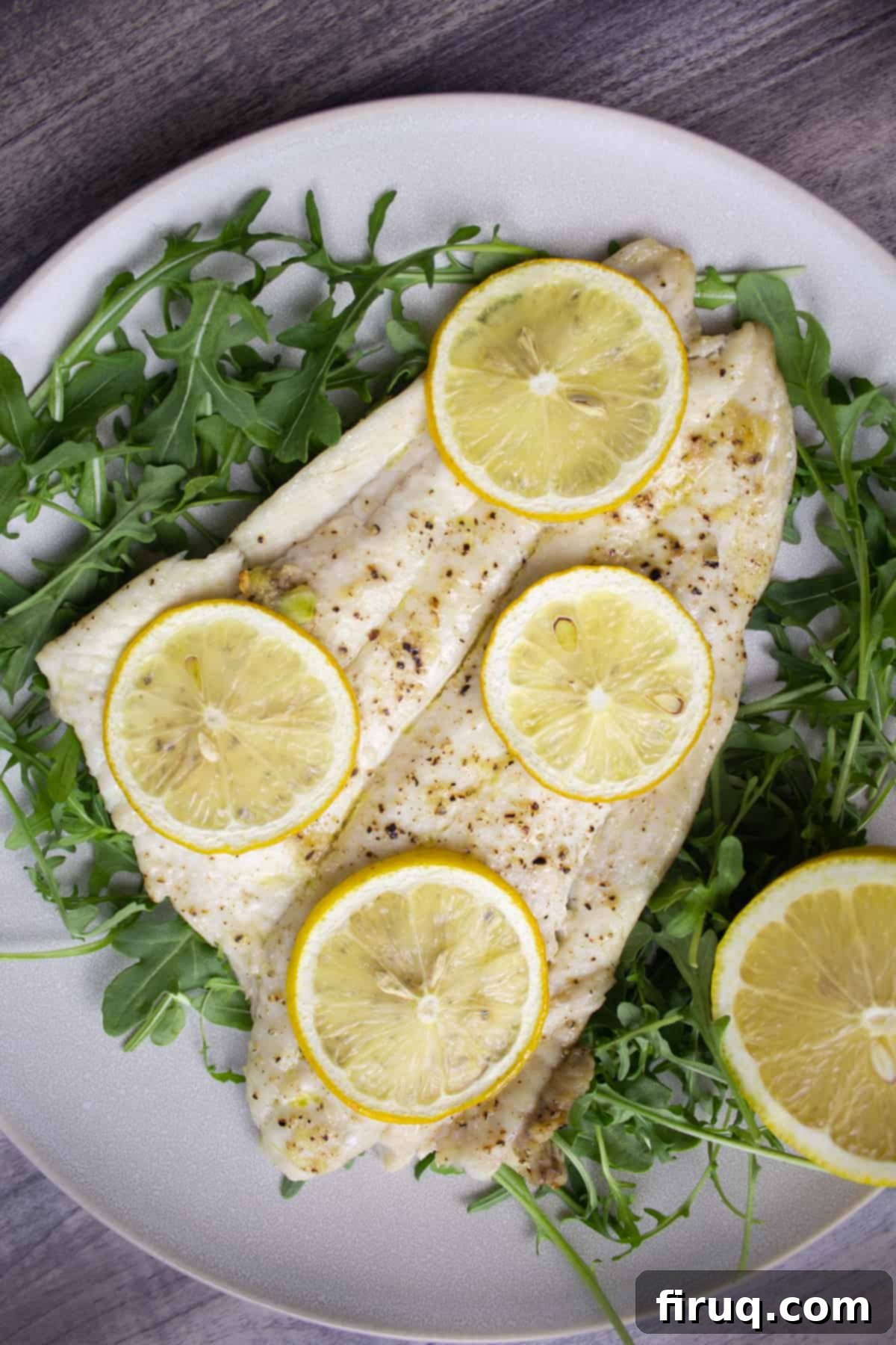 Bright Lemon Garlic Broiled Flounder 2 Broiled lemon garlic flounder served over a bed of fresh arugula, garnished with lemon slices, and seasoned with salt and pepper. The fish is golden brown and flaky.