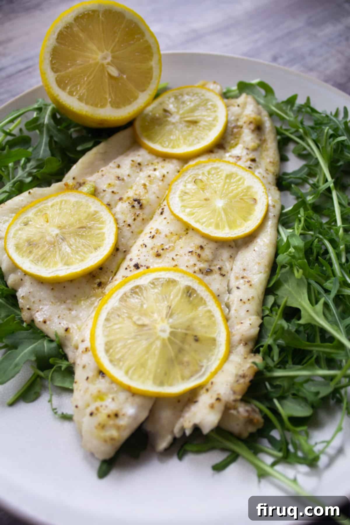 Bright Lemon Garlic Broiled Flounder 3 Close-up of a broiled flounder fillet topped with thin lemon slices, resting on a bed of fresh arugula, seasoned perfectly with salt and pepper.