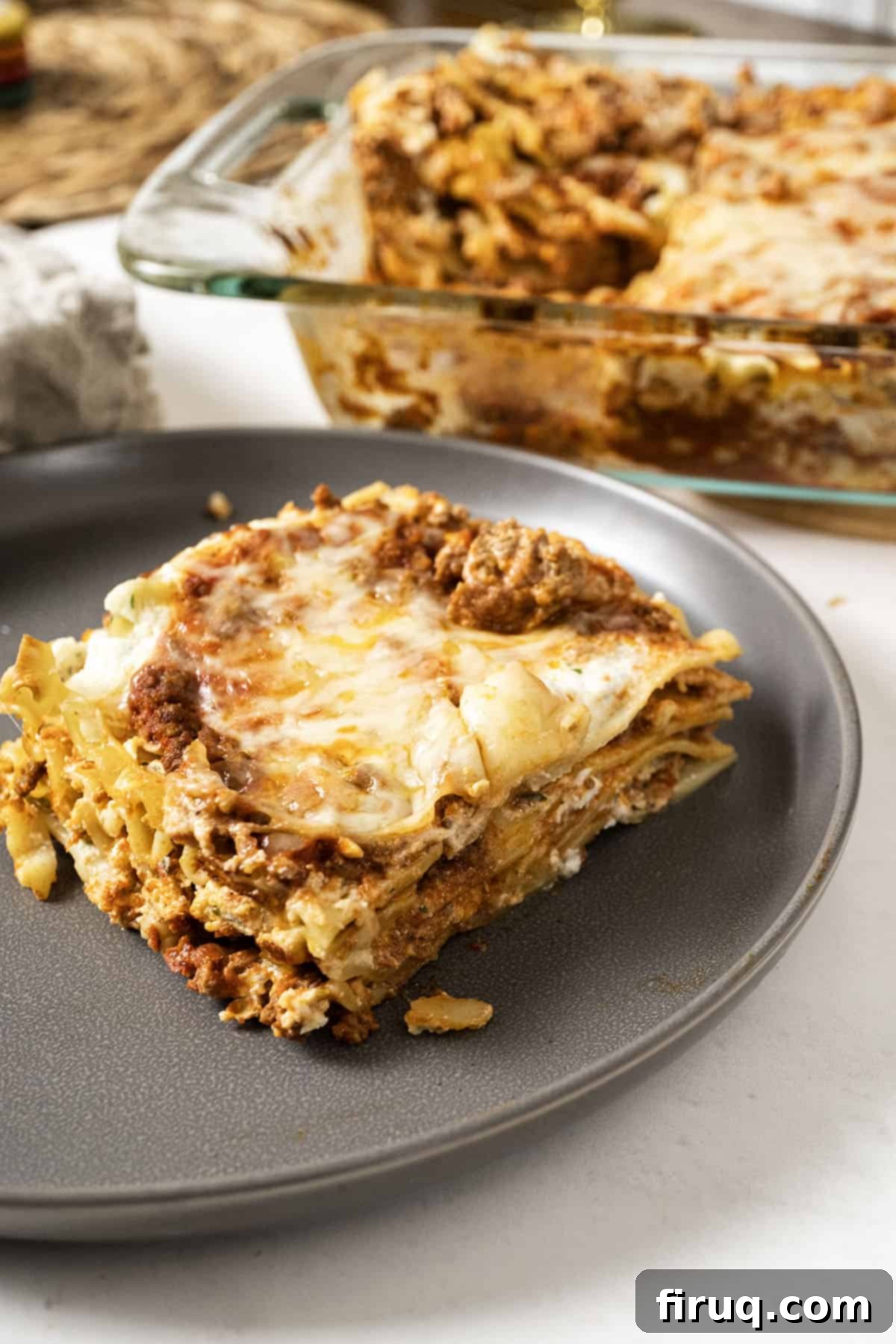 The Ultimate Homemade Italian Lasagna 2 A perfectly portioned square of authentic Italian lasagna on a white plate, with a large baking dish filled with more golden-brown lasagna in the background, ready to be served.
