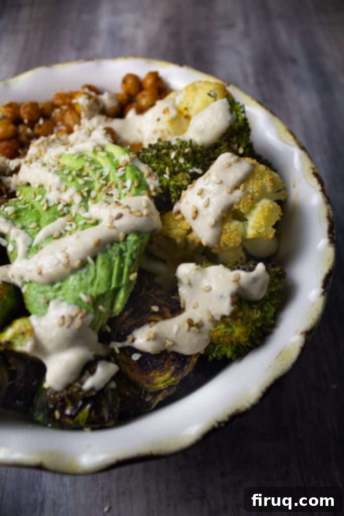 Crispy Chickpea Power Bowl 3 A close-up of a vegetable bowl topped with fresh avocado slices, creamy lemon tahini dressing, and a sprinkle of sesame seeds, ready to be enjoyed.