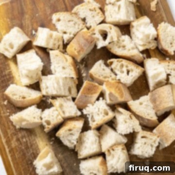 Crispy Homemade Parmesan Croutons 4 Chopped day-old Italian bread cubes scattered on a cutting board, ready for seasoning.