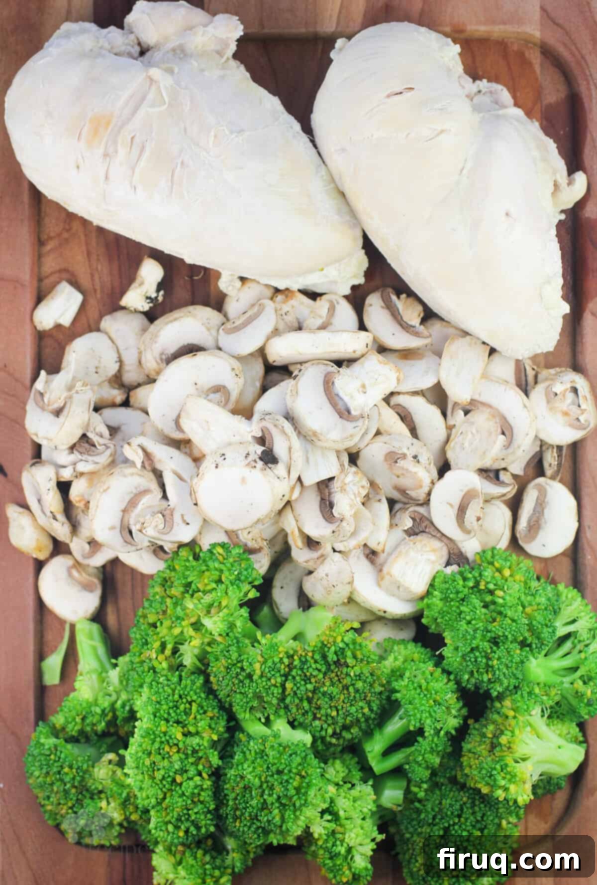 Creamy Chicken Broccoli Bake 3 A wooden board displays the raw ingredients for Chicken Divan: neatly arranged chicken breasts, sliced mushrooms, and vibrant green broccoli florets.