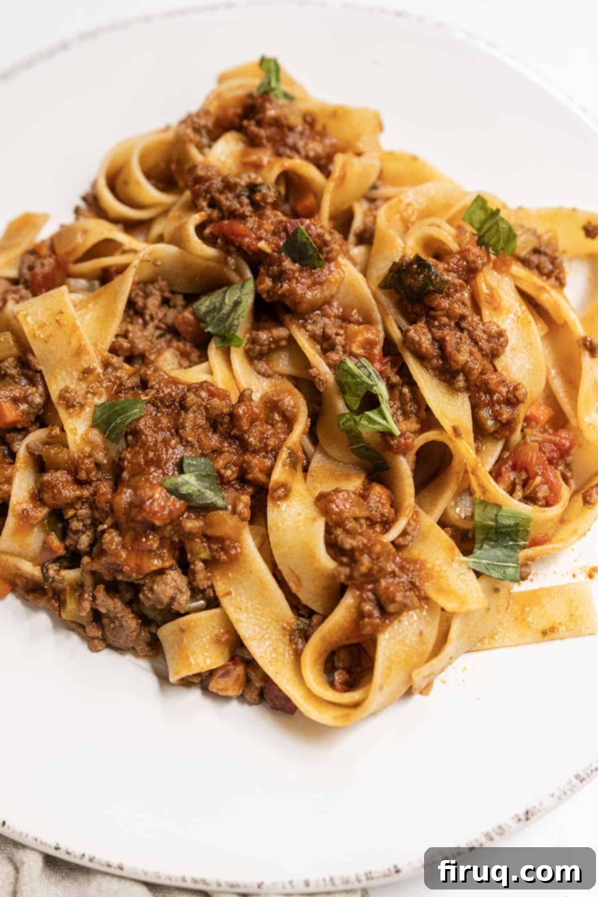 Classic Bolognese Ragù 2 Bolognese served over pappardelle on a plate, garnished with fresh basil and Parmesan.
