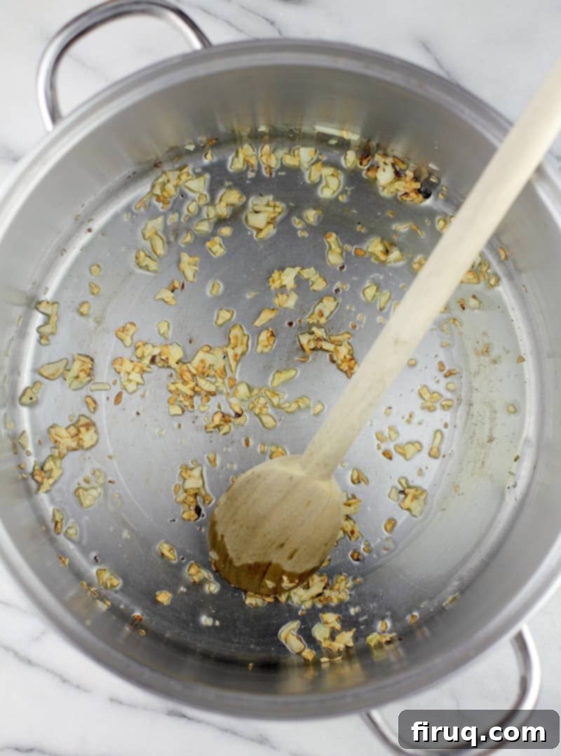 The Best Homemade Marinara 4 Top down view into a pot with a wooden spoon to show the browned garlic cooking