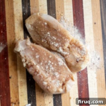 Creamy Chicken Tortellini Bliss 4 Seasoning raw chicken breasts on a cutting board with a mix of spices.