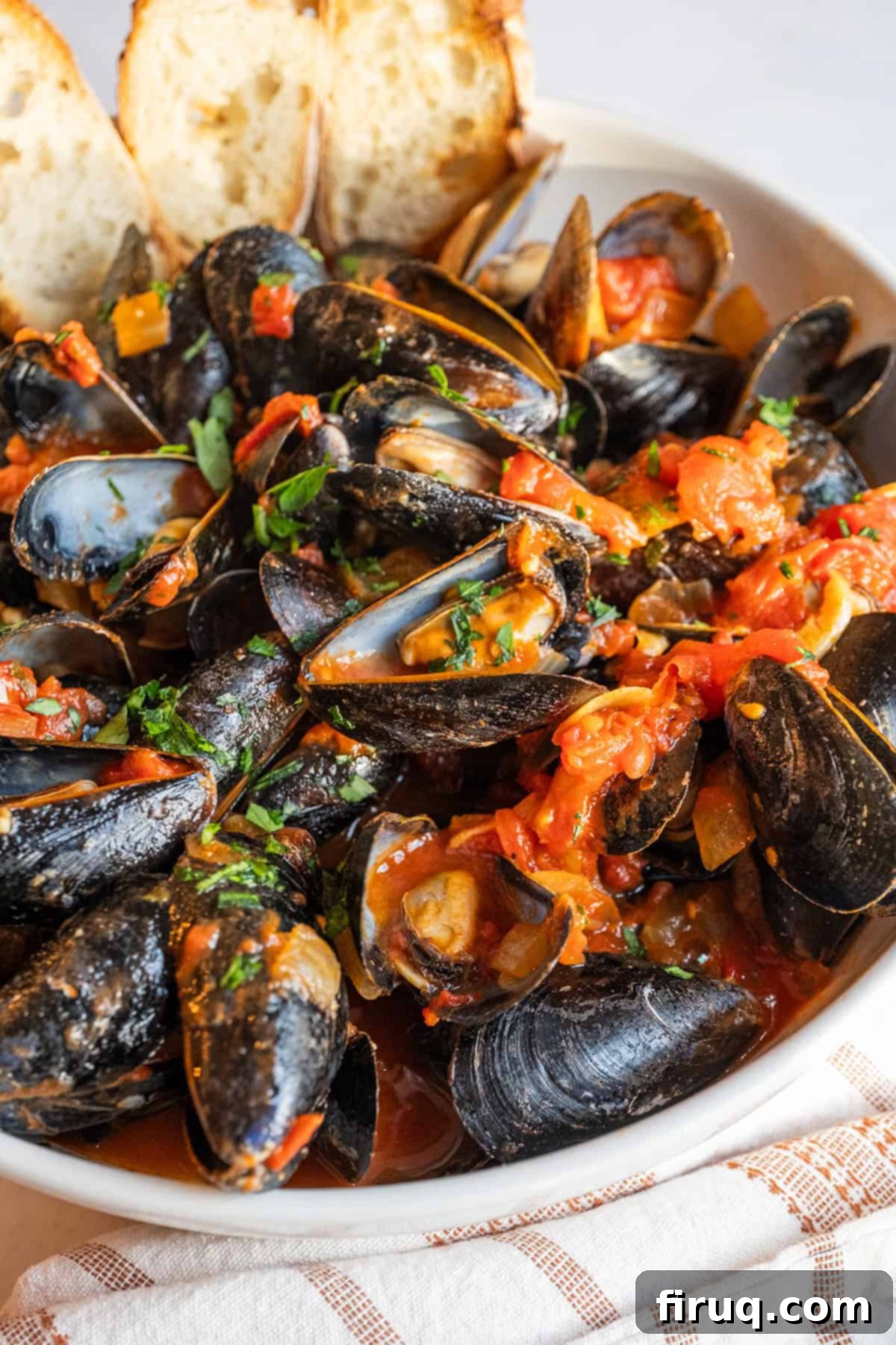 Devilishly Delicious Mussels 10 A close-up shot of a serving bowl filled with Mussels Fra Diavolo, showcasing the rich red sauce, open mussels, and fresh parsley, with crusty crostini ready for dipping.