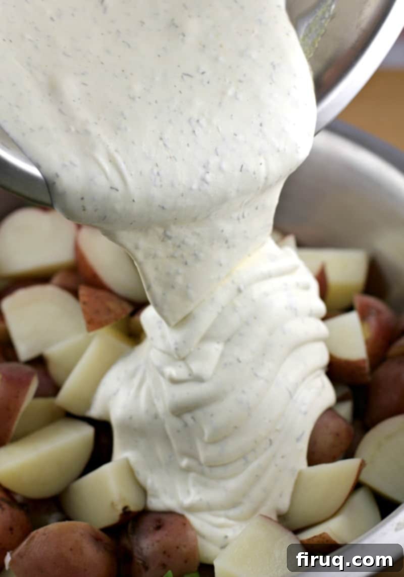 Spring Potato Salad with Zesty Dill 7 Creamy white dressing being poured over cooked red-skinned potatoes in a large bowl.