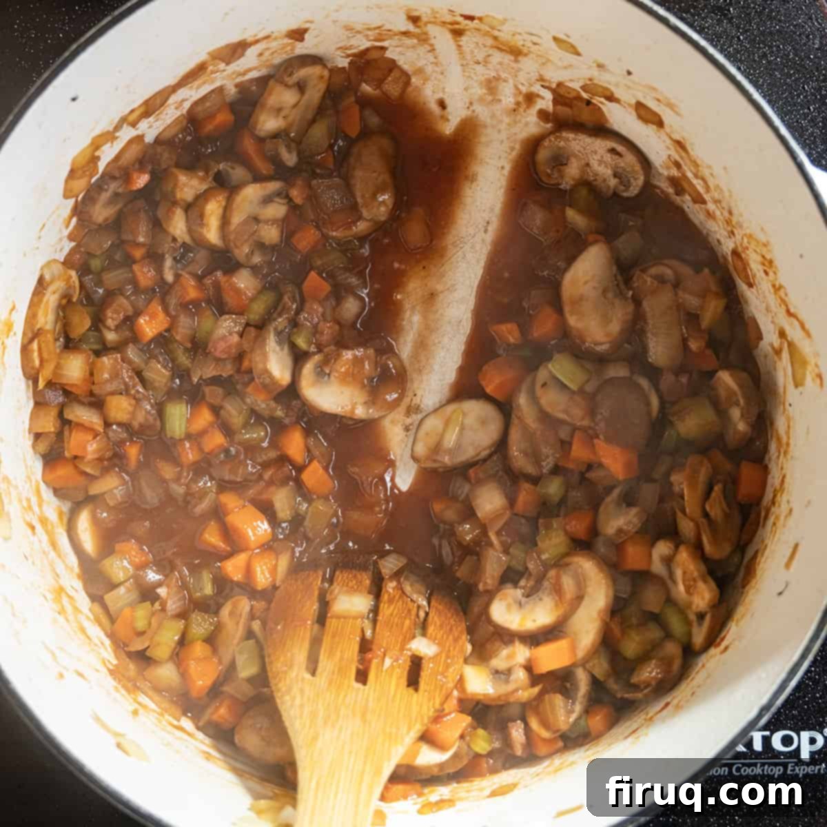Hearty Beef Barley and Mushroom Soup 7 A spoon demonstrates the thickness of reduced red wine in a pot with sautéed vegetables.