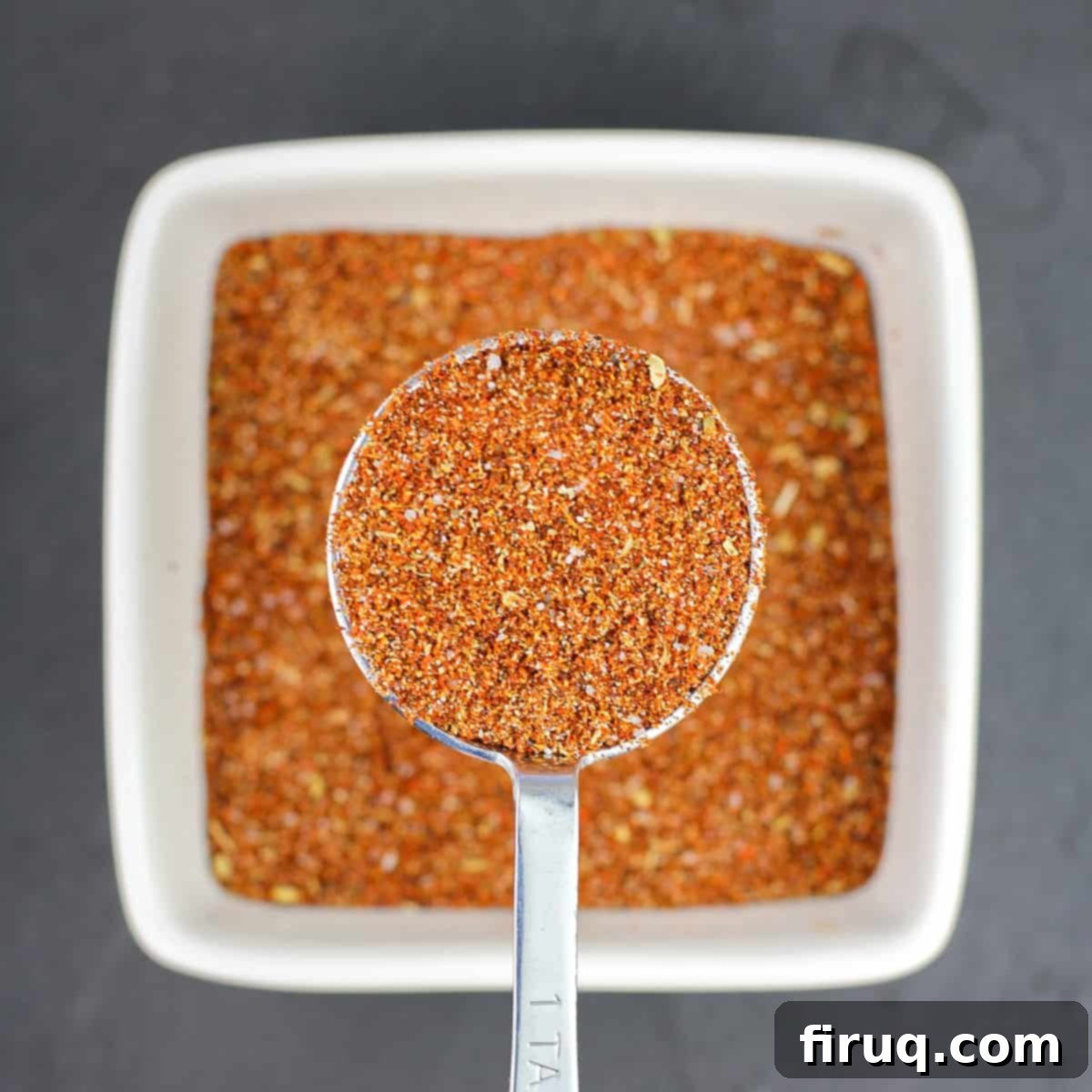DIY Taco Seasoning 4 measuring spoon holding homemade taco seasoning over white bowl filled with more seasoning