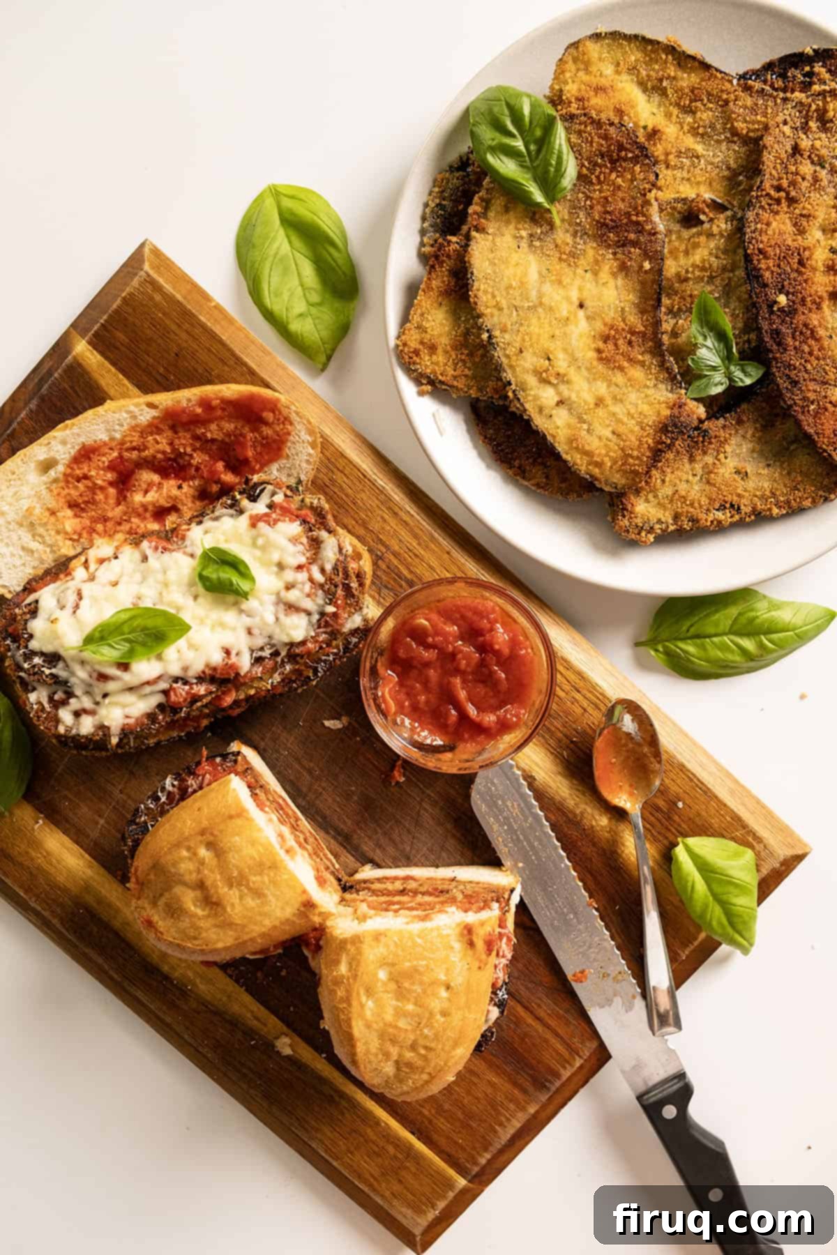 Eggplant Parmesan Sandwich 2 Two eggplant parm sandwiches on a cutting board with a plate of fried eggplant.