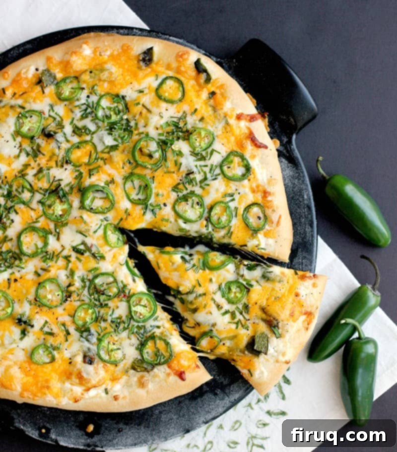 Popper's Paradise Pie 3 top view of the finished jalapeno popper pizza on a black pizza stone with a black background. a single slice is cut in the pizza and pulled out a bit.