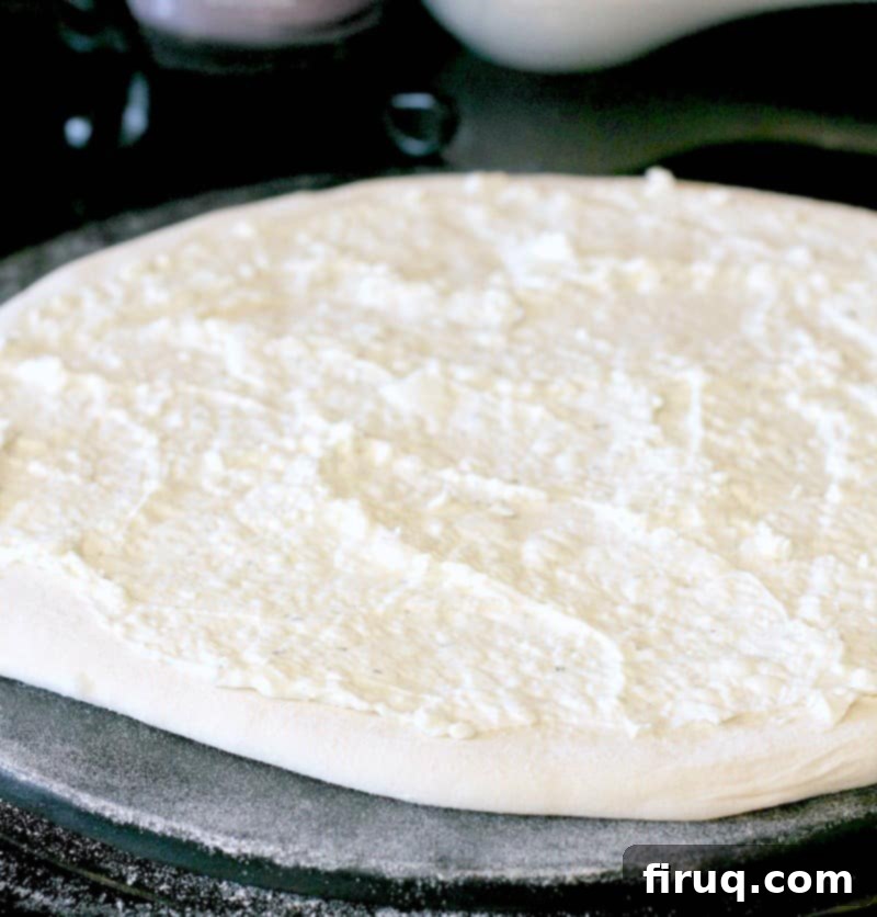 Popper's Paradise Pie 4 pizza dough rolled out on a stone, topped with the cream cheese sauce, the basis for the jalapeno cheese dip of this pizza