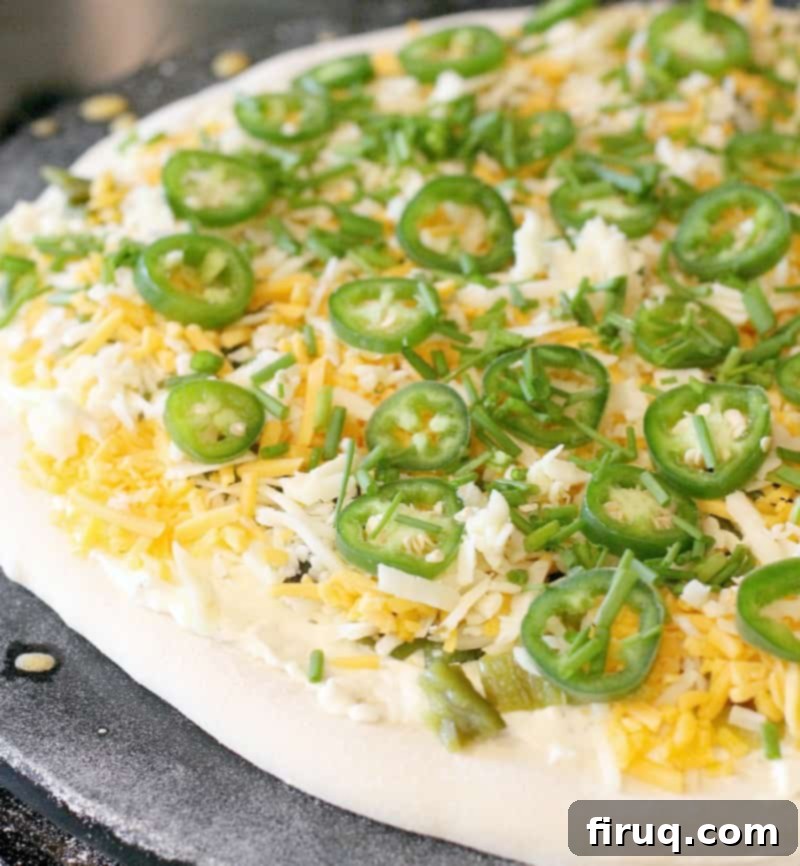 Popper's Paradise Pie 6 pizza dough rolled out on a stone, topped with the toppings ready for the oven