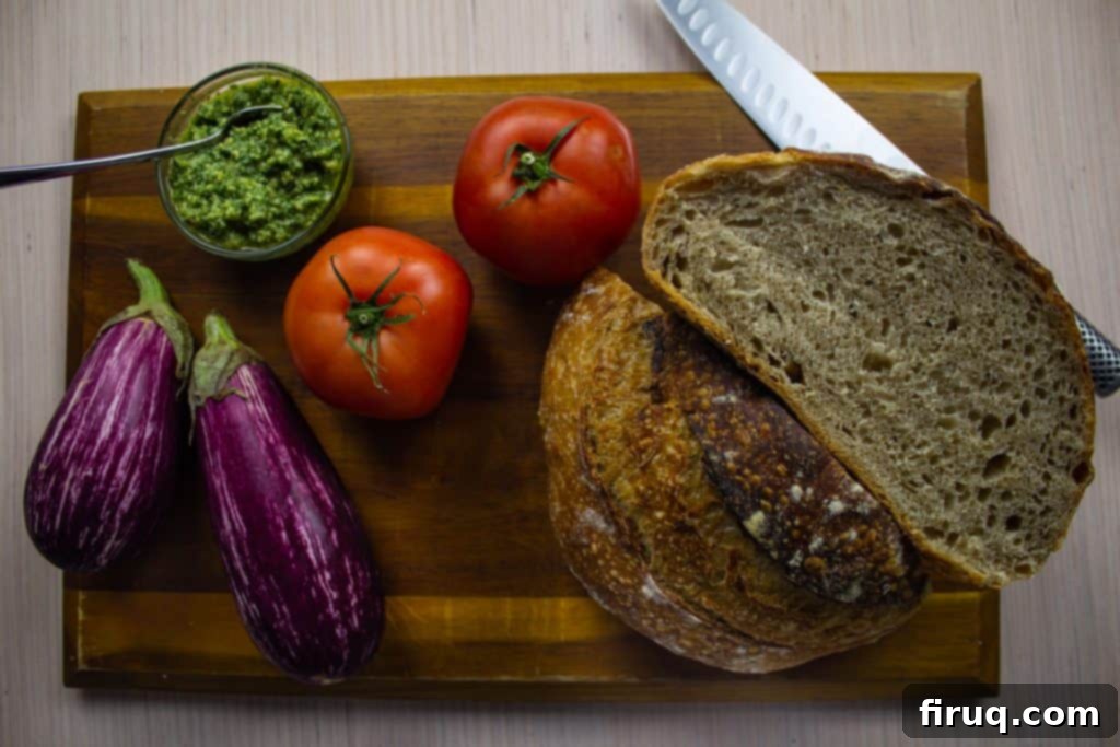 Ultimate Caprese Eggplant Melt 3 Fresh ingredients for Eggplant Caprese Grilled Cheese, including sliced eggplant, beefsteak tomatoes, a jar of pesto, mozzarella, and sourdough bread.