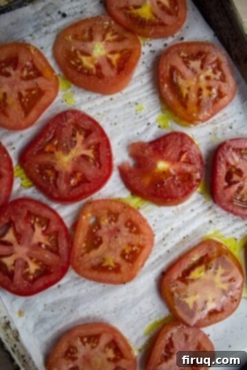 Ultimate Caprese Eggplant Melt 4 Thickly sliced beefsteak tomatoes seasoned with olive oil, salt, pepper, and garlic powder on a parchment-lined baking sheet, ready for roasting.