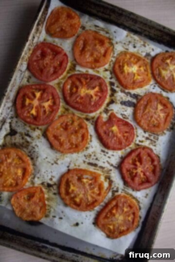 Ultimate Caprese Eggplant Melt 5 Perfectly roasted beefsteak tomatoes on a parchment-lined baking sheet, showing a deep red color after cooking.