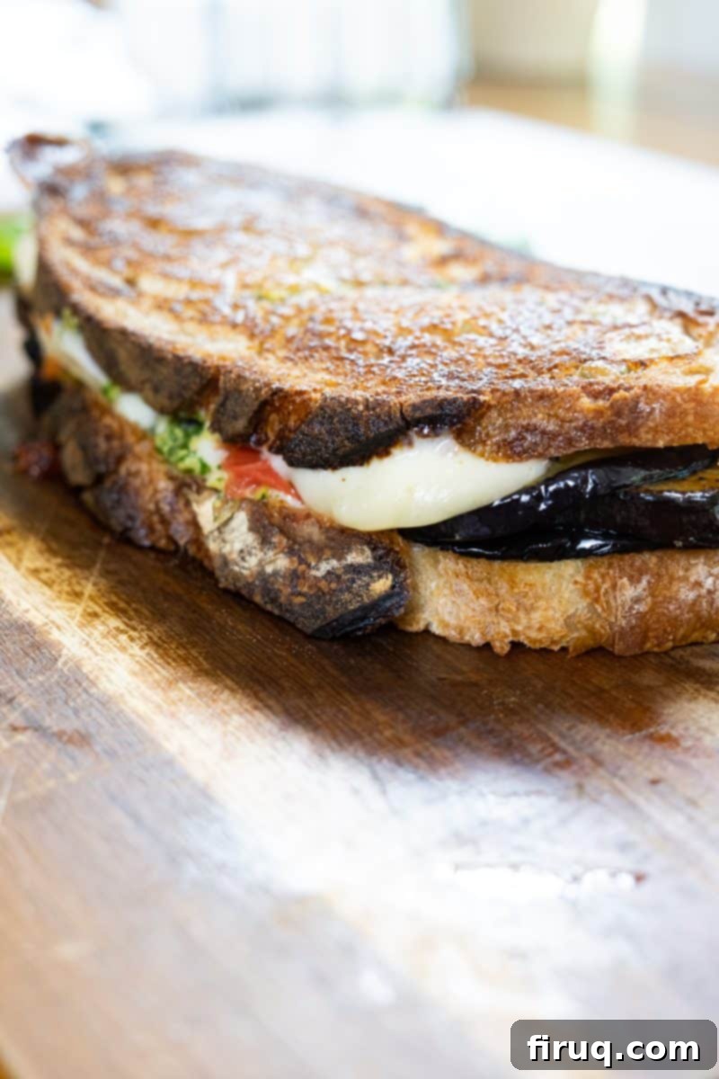 Ultimate Caprese Eggplant Melt 7 A freshly cooked Eggplant Caprese Grilled Cheese sandwich, cut in half and served on a rustic cutting board, ready to be enjoyed.