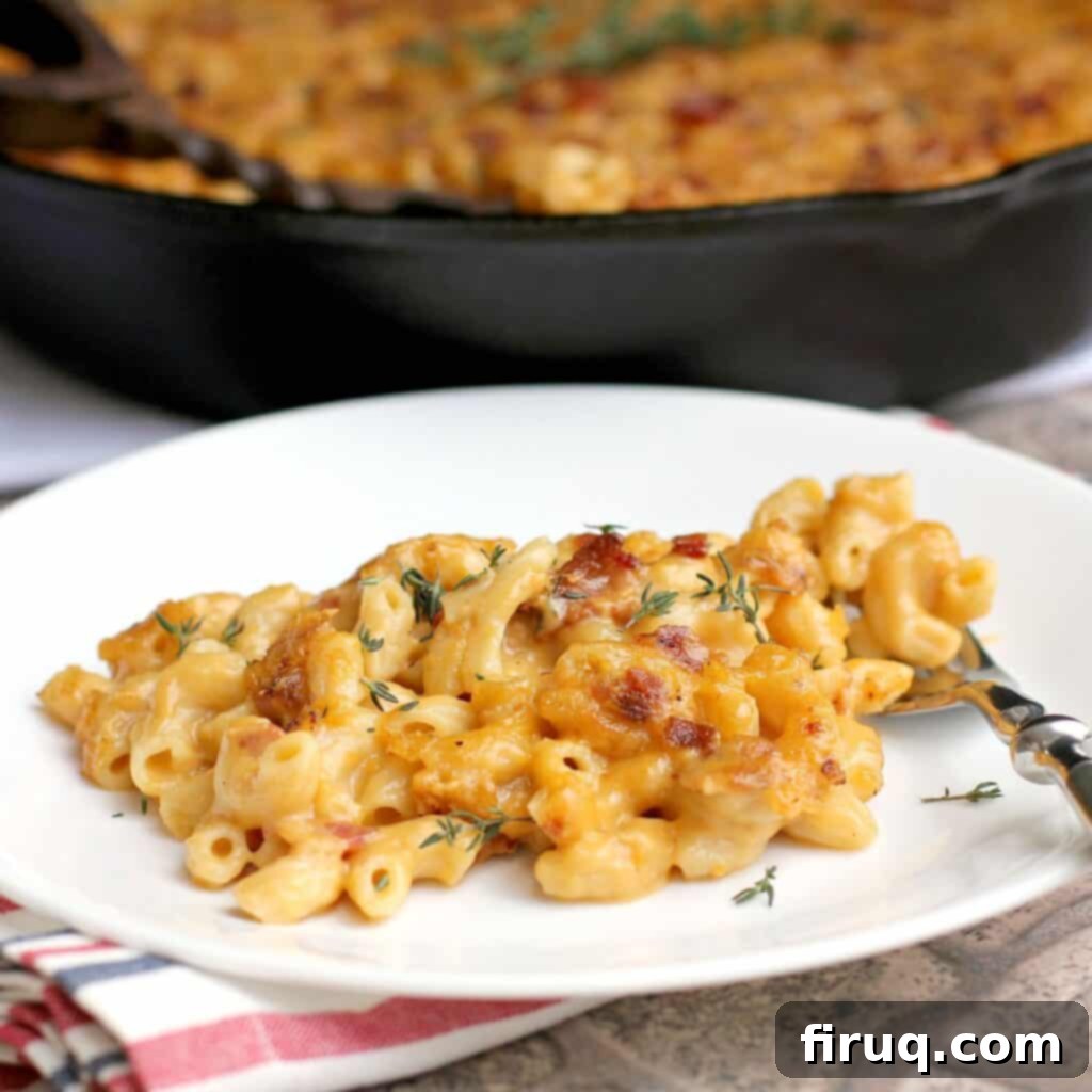Beer-Infused Bacon Garlic Mac & Cheese 2 side view of finished bacon macaroni and cheese plated on a white dish; remainder of the mac n cheese is in the background in a cast iron skillet (zoomed view)