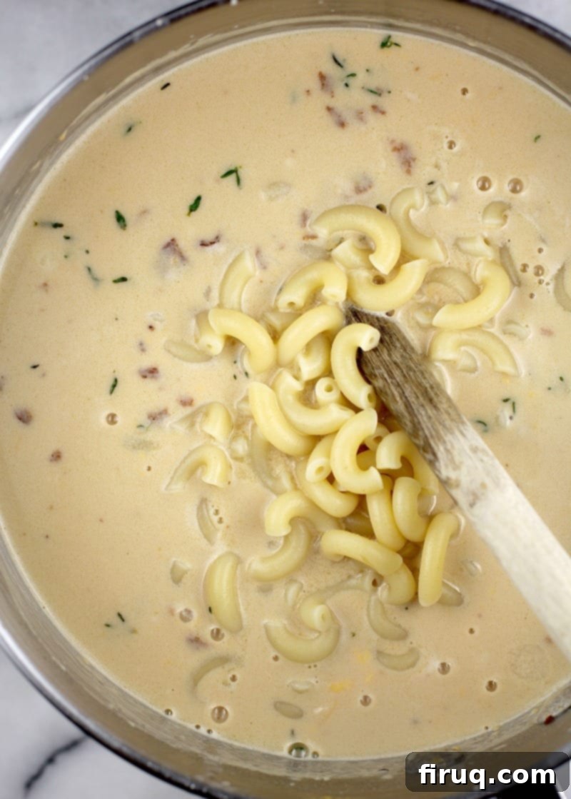 Beer-Infused Bacon Garlic Mac & Cheese 8 macaroni being added to the cheese sauce, top down view in a saucepan